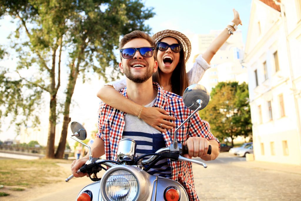 Junges Paar fährt fröhlich lachend auf der Vespa durch die Stadt