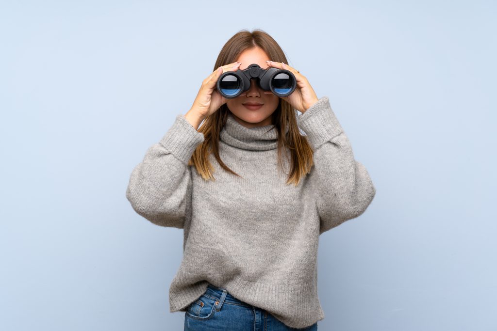 Junge Frau mit Fernglas blickt suchend nach Vorne